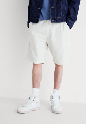 Light-colored cotton shorts with an elastic waistband, paired with white athletic sneakers and ribbed white socks. Denim jacket on top.