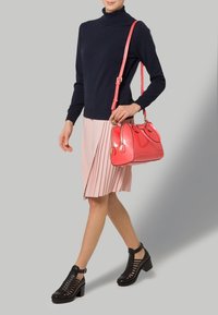 Rosa plisserad kjol, marinblå polo, svarta öppna klackskor med blockklack, och en glansig korallhandväska med dubbla handtag och rem för att bära över kroppen.