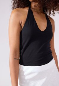 Sort ærmeløs top med dyb V-hals, lavet af blødt stof, med en tætsiddende design og glat tekstur, parret med en hvid nederdel.