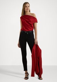 Röd off-the-shoulder topp i satin, kombinerad med svarta skinny jeans och en röd kavaj. Modellen bär svarta remsandaler.