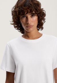 Hvid bomulds t-shirt med korte ærmer og rund halsudskæring, der har en glat tekstur og et enkelt design. Ingen bemærkelsesværdige mønstre eller accenter.