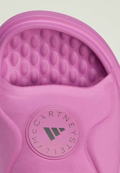 Pink slide sandal featuring a textured upper with a raised dot pattern, a rubber logo patch, and a curved, open design.
