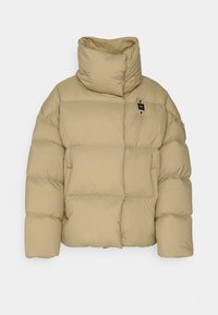 Beige vadderad jacka med hög krage och quiltad textur. Har en liten logotypetikett och en överdimensionerad silhuett. Tillverkad av ett mjukt, isolerande material.