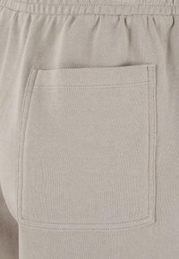 Gros plan sur un pantalon en tissu beige avec une taille élastique et une poche arrière rectangulaire cousue.