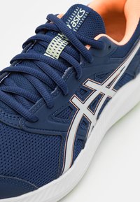 Zapatilla deportiva ASICS de color azul marino con acentos en rosa, suela blanca, franjas de logo blancas y cordones en azul marino sobre un fondo blanco.