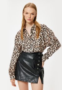 Blouse à imprimé léopard avec un devant à boutons et des manches amples, assortie à une jupe en faux cuir noir taille haute avec des boutons sur le côté.