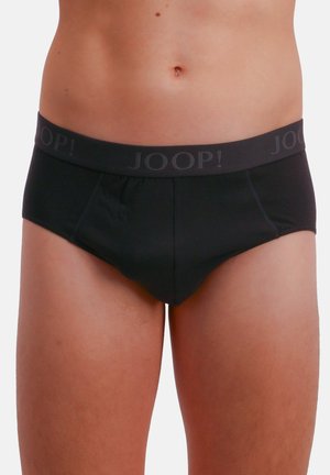Torse masculin portant un slip noir avec le logo "JOOP!" sur la ceinture, sur un fond clair uni.