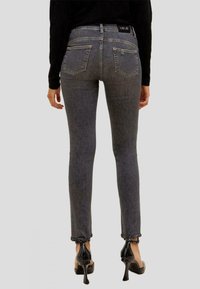 Jeans de denim negro ajustados con un acabado ligeramente desgastado, que presentan bolsillos traseros y dobladillos deshilachados, combinados con zapatos de tacón negros.