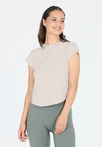 Helles beige Kurzarmoberteil mit rundem Ausschnitt und abgerundetem Saum, kombiniert mit grünen Leggings, die eine glatte Textur und einen lässigen Schnitt aufweisen.