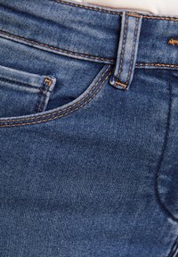 Blaue Jeans aus Denim mit kontrastierendem Nähen, einer Vordertasche und einem klassischen Knopfverschluss. Der Stoff hat eine glatte Textur.