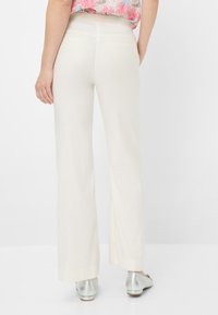 Witte, wijde pantalons met een gladde textuur, voorzien van twee achterzakken. Gecombineerd met zilveren, lage hakken.