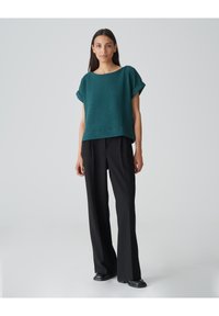 Teal textuur gebreid topje met omgeslagen mouwen, gecombineerd met zwarte high-waisted broek. De outfit heeft een relaxte pasvorm en een minimalistisch ontwerp.