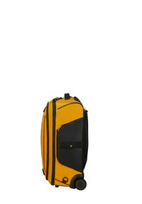 Valise à roulettes jaune et noire, positionnée verticalement, avec plusieurs compartiments zippés et une poignée rétractable sur un fond blanc.