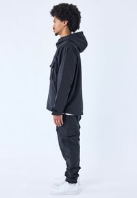 Chaqueta negra con capucha y bolsillos frontales, combinada con pantalones cargo a juego. Ambos hechos de una tela suave y duradera; cuentan con puños elásticos y remates en los tobillos.