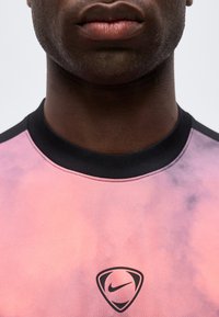 Κοντινό πλάνο ενός ατόμου με ροζ και μωβ διαβαθμισμένη μπλούζα Nike με μαύρο γιακά, όπου φαίνονται τα χείλη και το κάτω μέρος του προσώπου.