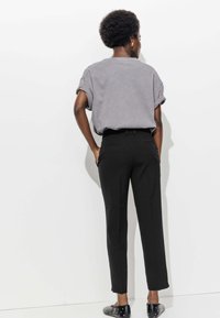 T-shirt gris à manches retroussées, pantalon noir ajusté avec poches, et ballerines noires avec clous blancs. Fond uni.