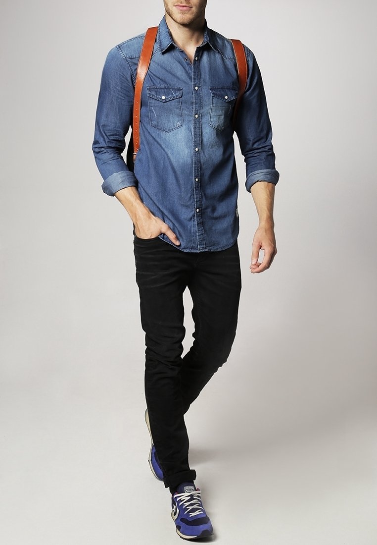 Farkkupaita, jossa on kaksi rintataskua, käännetyt hihat ja ruskeat nahkaiset olkahihnat. Mustat slim fit -housut ja siniset lenkkarit täydentävät asun.