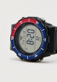 Digitálne športové hodinky s čiernym puzdrom, červeným a modrým rámikom, veľkým LCD displejom a tlačidlami na funkcie osvetlenia a režimu. Vodotesný dizajn.