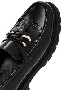 Mocasín de cuero negro con un detalle de flecos texturizados, acentos de hardware en tono dorado y una suela de goma gruesa para mayor durabilidad.