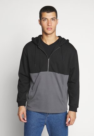 Svart og grå hettegenser med glidelås foran, med delt design. Laget av mykt stoff med kengurulomme og justerbar snorhette.