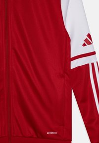 Rode polyester ritsjack met witte accenten, gestructureerde stof en "AEROREADY" branding nabij de zoom, en gedurfde drie strepen op de mouw.