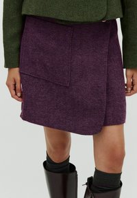 Lila, texturerad ullkjol med en omslagsdesign och en stor frontficka, tillsammans med knähöga glansiga bruna stövlar och mörkgrå strumpor.