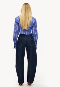 Camisa de manga larga a rayas azules y blancas, diseño corto; pantalones de mezclilla oscuros de pierna ancha con bolsillos traseros, textura lisa y líneas de costura visibles.