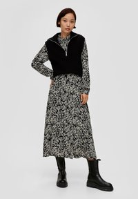 Schwarzes geripptes Top über einem langärmligen Blumenkleid mit einem weißen abstrakten Muster, kombiniert mit kniehohen schwarzen Stiefeln.