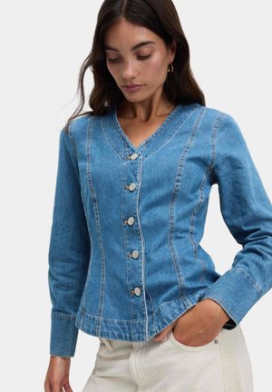 Lyseblå denimjakke med V-hals, fem sølvknapper og lodrette sømme. Har lange ærmer og en rynket kant.