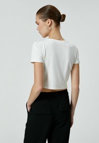 Valkoinen lyhythihainen cropped T-paita, joka on valmistettu pehmeästä puuvillasta. Yhdistetty mustiin housuihin, joissa on käytännölliset läppätaskut ja muotoiltu istuvuus.