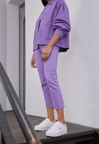 Veste en denim violette et pantalon assorti avec une coupe décontractée. Baskets blanches avec des accents gris subtils. Texture lisse, design décontracté.