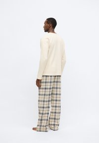 Világos bézs hosszú ujjú felső texturált anyagból, bézs, fekete és tengerészkék kockás bő szárú nadrággal párosítva. Díszítések nélküli kialakítás és kényelmes szabás.