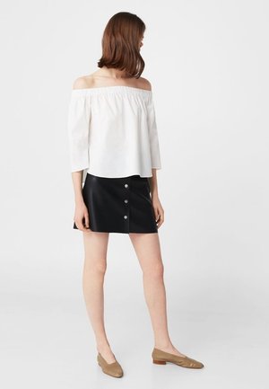 Blusa bianca scollata sulla spalla con maniche a tre quarti, abbinata a una mini gonna nera in similpelle con dettagli di bottoni frontali.