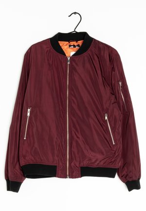 Veste bomber bordeaux avec col, poignets et bord noir, dotée d'une fermeture éclair à l'avant, de deux poches zippées et d'une doublure intérieure orange, suspendue à un cintre.