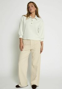 Light gray pullover with a collar and three buttons, paired with high-waisted beige wide-leg pants. Soft texture, casual design.
