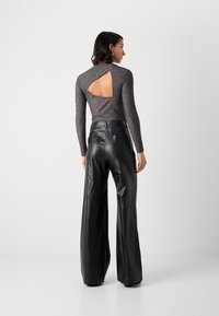Pantalons large en cuir noir avec une texture lisse, associés à un haut gris ajusté avec une découpe dans le dos et un design côtelé.