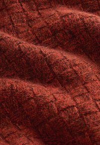 Tekstūruota medžiaga tamsiai raudonos spalvos su žąsies kaulo raštu, pasižyminti minkštu, pūkuotu paviršiumi ir subtiliais spalvos bei gilumo variacijomis.