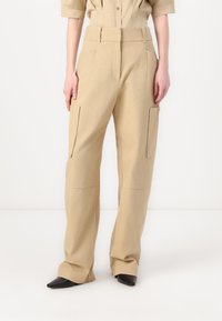 Beige cargo pants featuring a high waist, wide legs, and front pockets. Made from a sturdy fabric with a smooth texture.