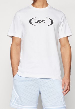 Homme portant un T-shirt blanc à manches courtes avec un logo Reebok noir et un short de sport perforé bleu clair avec bordure blanche.