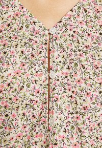 Blusa floral de botonadura con escote en forma de V. Presenta una tela ligera en color crema, decorada con flores rosas y verdes, y un detalle de botón en el centro.