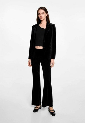 Černý sametový blazer s jedním knoflíkem, kombinovaný s černým crop topem a rozšířenými černými kalhotami. Vyznačuje se hladkou texturou a přizpůsobeným střihem.