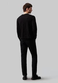 Svart strikkegenser med rund hals, kombinert med svarte bukser. Outfiten har en tettsittende design og glatt tekstur.