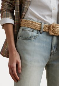 Lyseblå denimjeans med et flettebelte i beige med firkantet spenne. Antrekket inkluderer en rutete blazer med en hvit skjorte under.