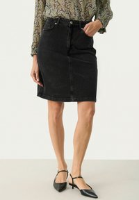 Črna denim krilo z oprijetim pasom, gumbom za zapiranje in sprednjim žepom. Gladka tekstura, do kolen, z detajli šivanja. Nošeno z črnimi čevlji.