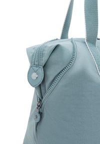 Light blue nylon bag with a zip closure. Features a looped zipper pull and a round metal accent. Textured surface and sturdy handles.