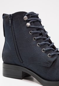 Stivaletto blu navy con finitura testurizzata, dotato di zip laterale, occhielli in metallo, lacci e tacco in gomma nera.