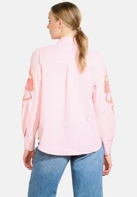 Ilga rankovė, rausvos spalvos dryžuota palaidinė su gėlių siuvinėjimu ant rankovių, minkšta medžiaga, laisvo kirpimo ir susegamomis rankogaliais. Kasdienio stiliaus dizainas.