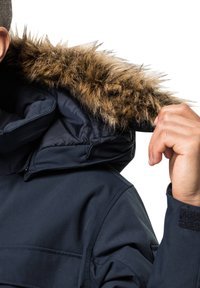 Veste bleu marine avec un design matelassé et une capuche en fausse fourrure. La fourrure est de teintes marron, ajoutant de la texture au vêtement.