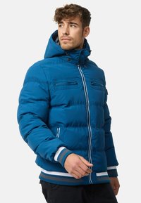 Blue puffer jacket with a hood, front zipper, and two chest pockets. Features ribbed cuffs and waistband with contrasting stripes.