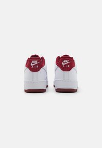 Biele tenisky s červenými akcentmi a štruktúrovanou gumovou podrážkou. Na zadnej strane sa nachádza výrazné logo "Nike Air". Klasický nízky strih.